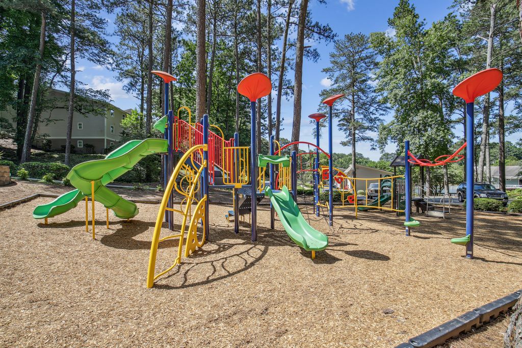 Outdoor playgound with slides surrounded by naitve landscaping with apartment buildings in background.